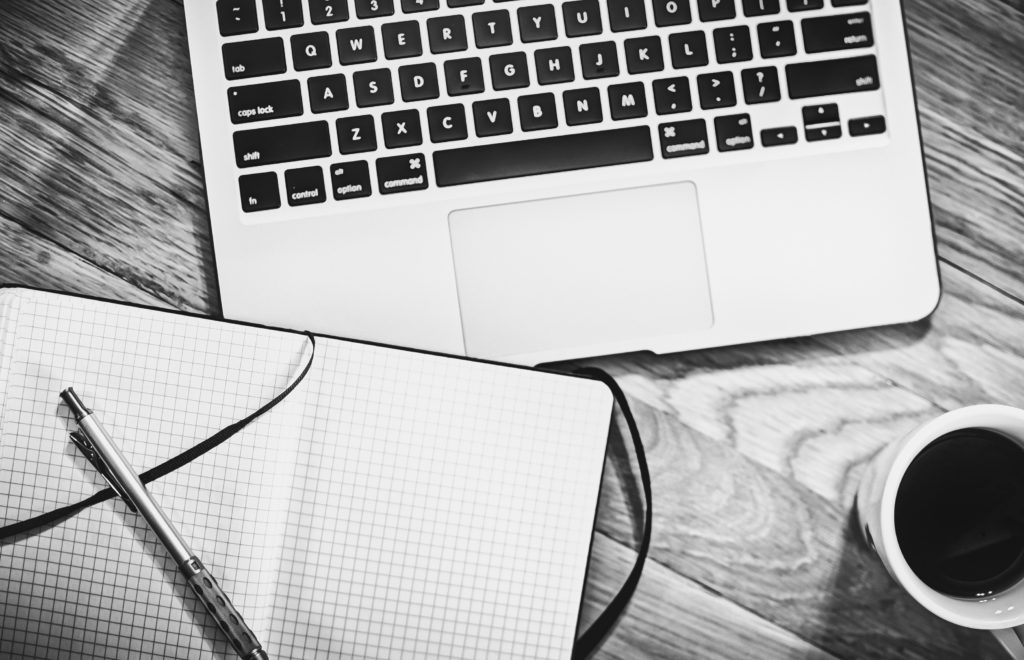 Notizbuch, Stift, Laptop und Kaffee auf einem Holztisch